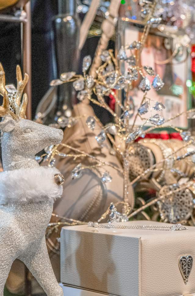 store holiday display of of white and sparkly deer with fur collar and gold antlers stands before display of shiny bracelets and leather purse and box