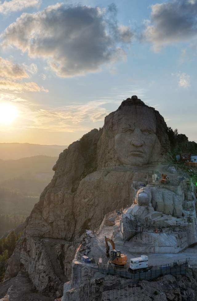 looking straight on at Crazy Horse memorial with the sun setting and black hills behind the statue