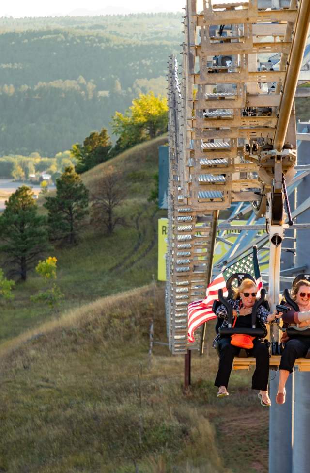 two riders on the buffalo hunt coaster with green hills in the background at fort hays in rapid city sd