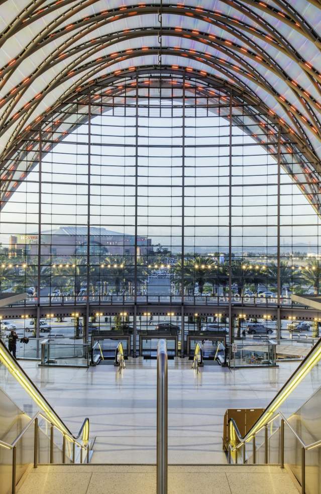 Anaheim Regional Transportation Intermodal Center modern interior with sleek escalators and panoramic glass wall showcases palm trees and cityscape outside.