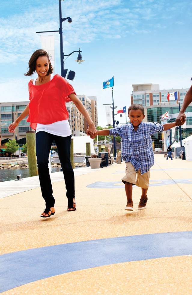 A family of 3 holding hands walking along the National Harbor Pier
