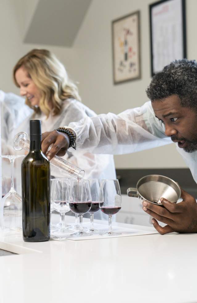 A group of people in lab coats are blending wine with glass tubes