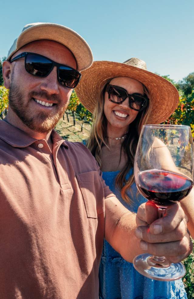 Guy and girl with wine glasses and red wine in vineyard