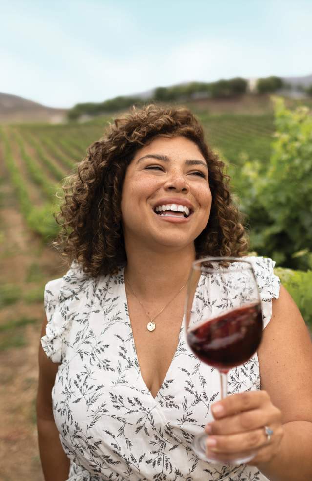 A woman enjoying at glass of red wine among the vineyards.