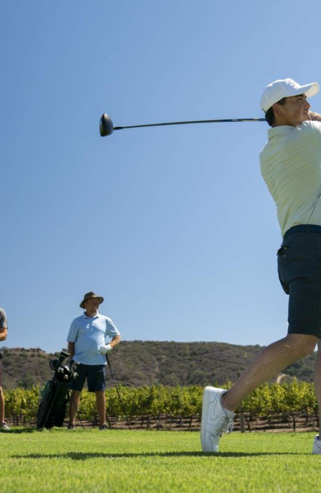 A man swings a golf club on the course while others watch