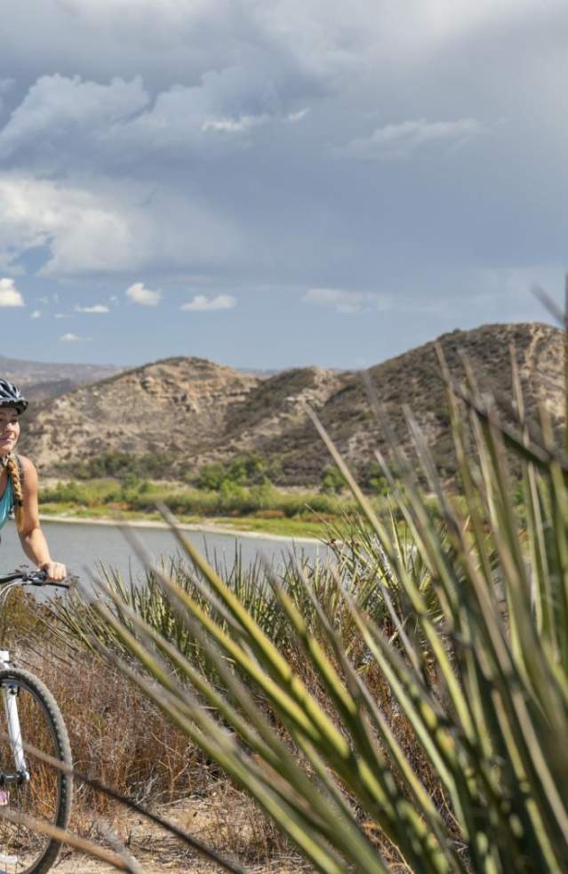 A woman and a man ride mountain bike through a trail near a lake