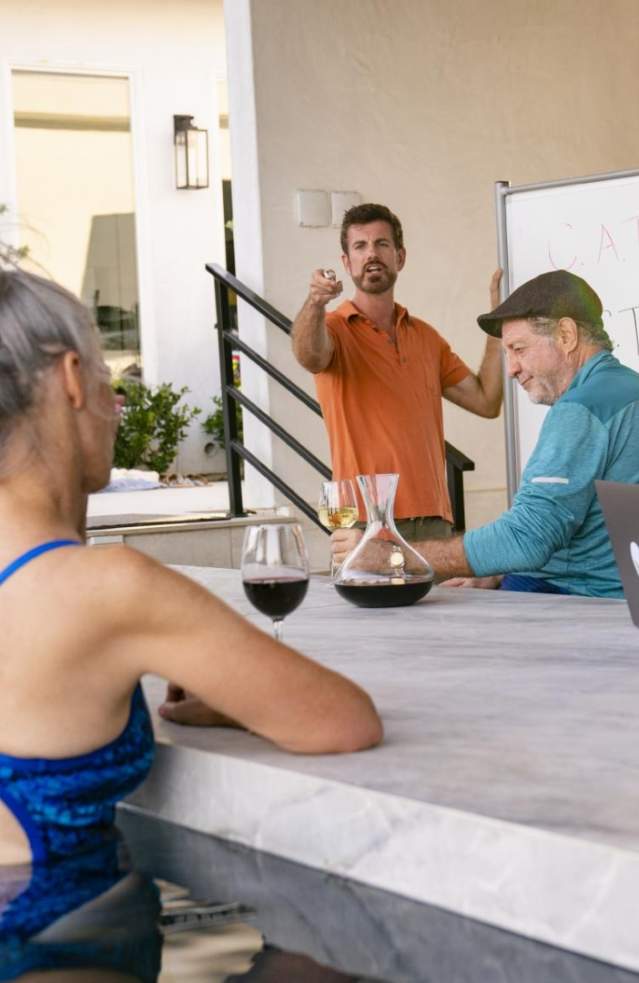 Several people sit by the pool enjoying a glass of wine