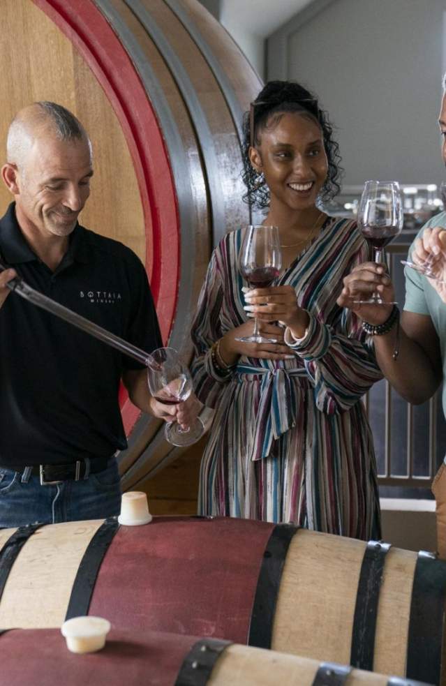 Several people enjoy a wine tasting while a winemaker explains the process