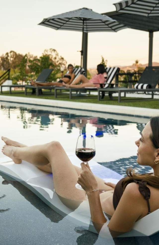 A woman relaxes by the pool with a glass of red wine