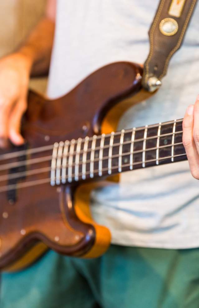 A close up of a guy strumming a brown guitar.
