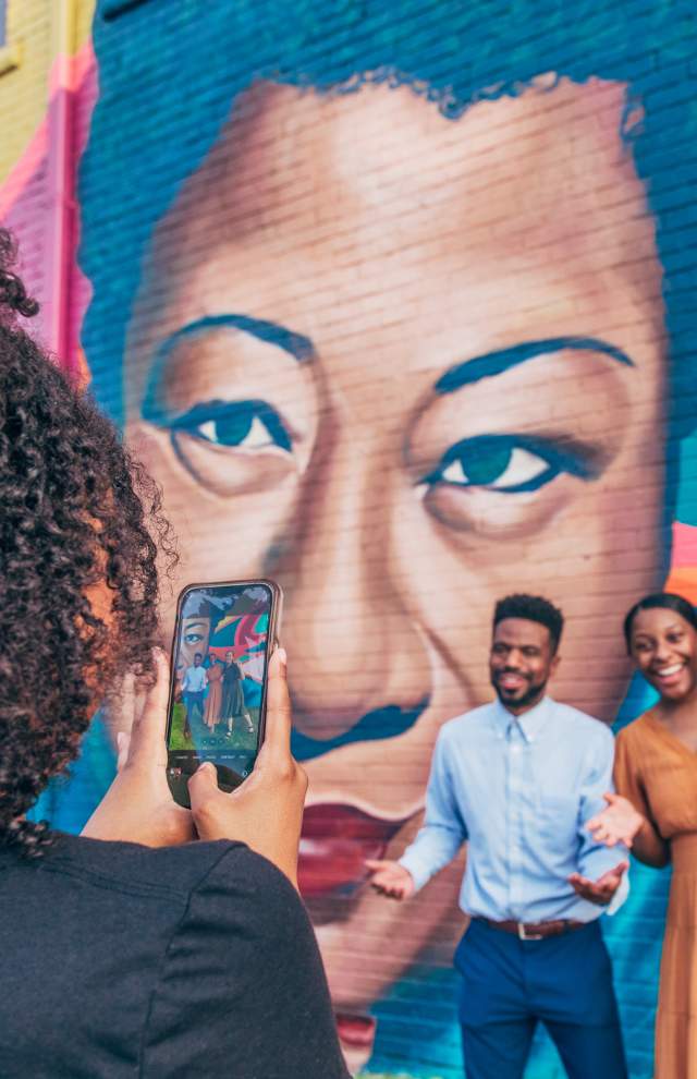 3 Friends Pose in front of Street Art mural while a person takes a photo