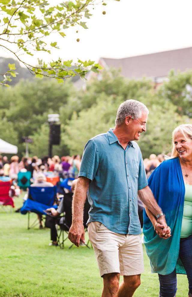 Couple holding hands at summer concert with gazebo stage in background
