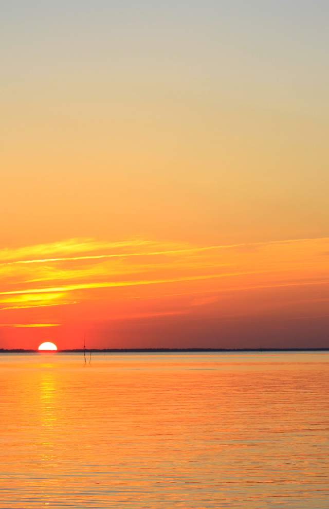 Skiff sailing on reflective river during an orange sunset