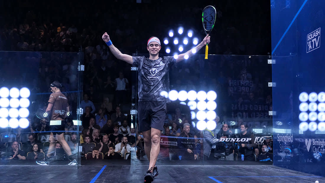 Squash player standing in play area holding arms and  racquet in the air in victory