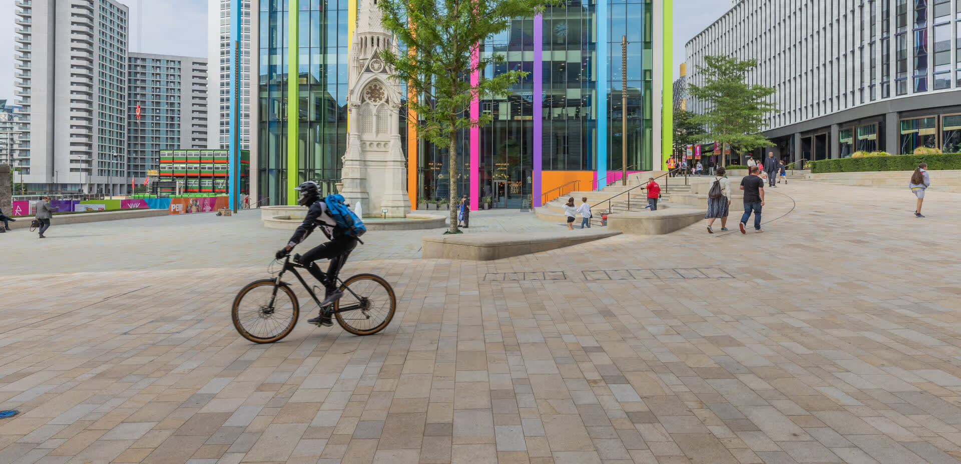 A cyclist crosses in front of the fountain in Paradise, Birmingham, with city dressing for the 2022 Commonwealth Games in the background