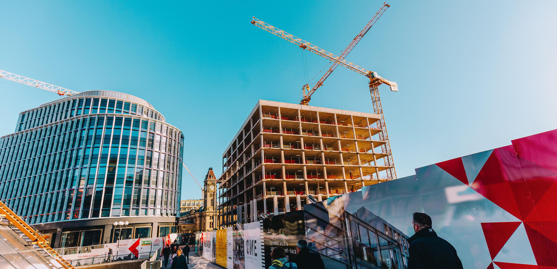 Cranes tower over the development in Paradise, Birmingham, as pedestrians walk below.