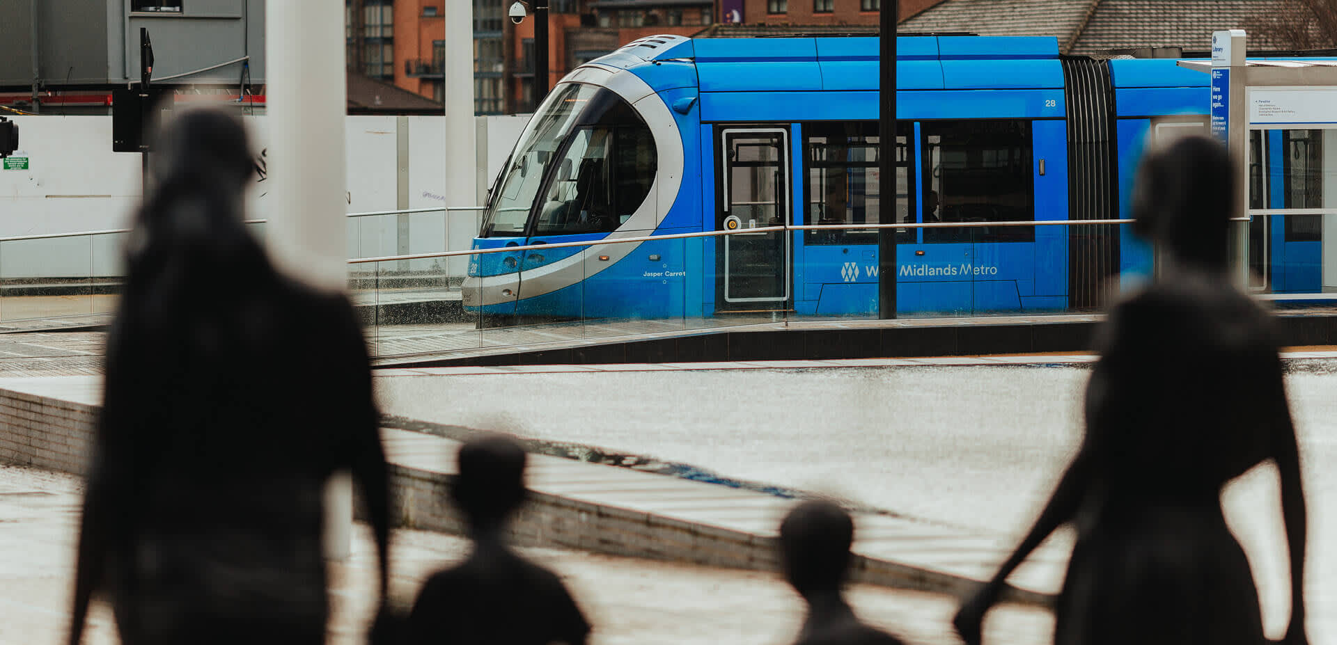 A tram is seen in the distance, past the silhouette of a family of statues