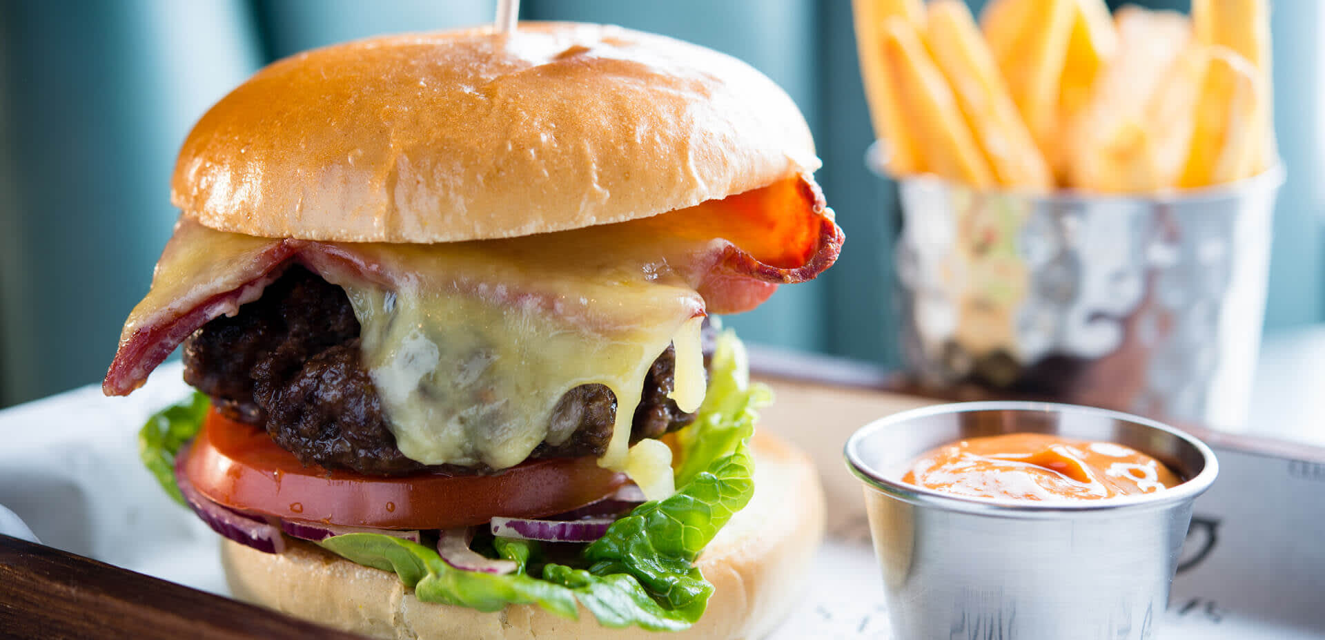 Close up photo of a stacked cheeseburger on a plate, alongside ranch dressing and fries