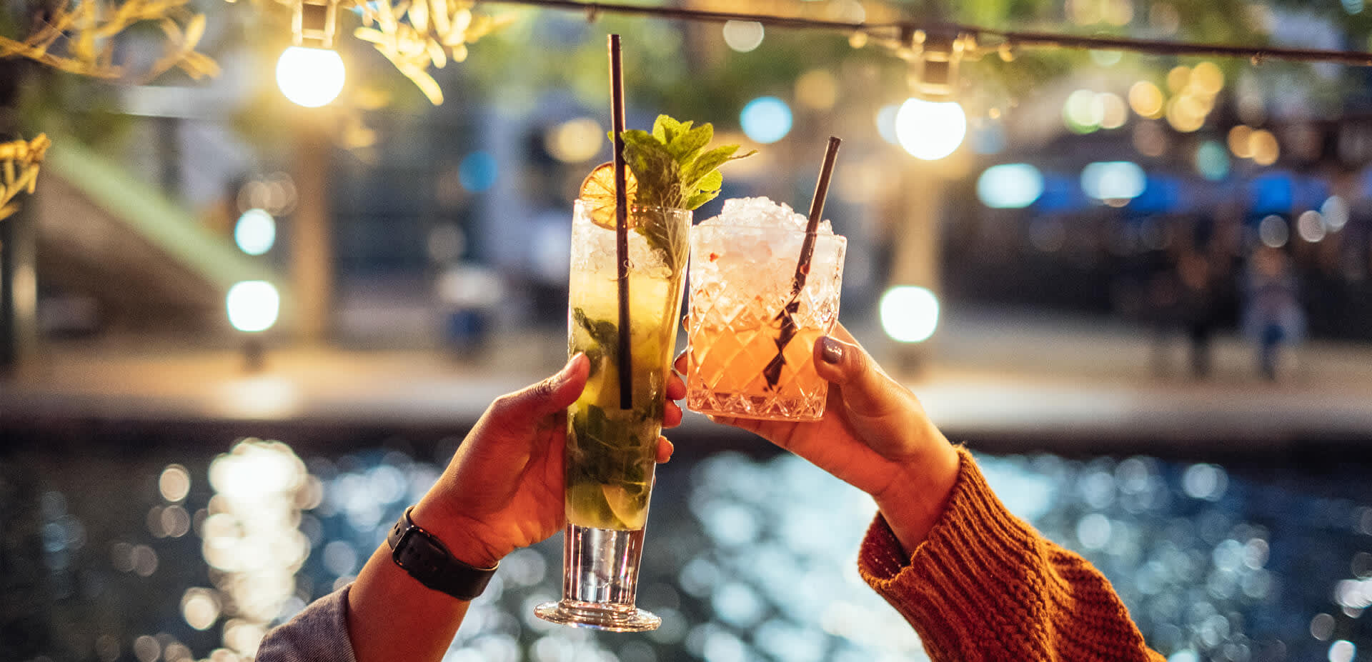 Two people raising cocktails in the air to cheers