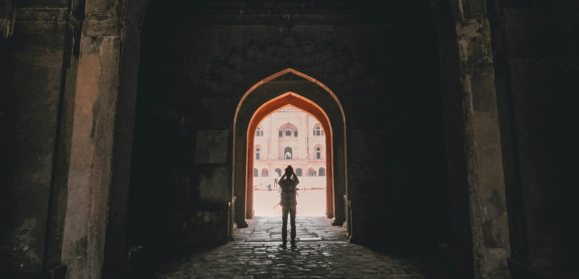 A tourist stands silhouetted in a bright archway at a historical site.