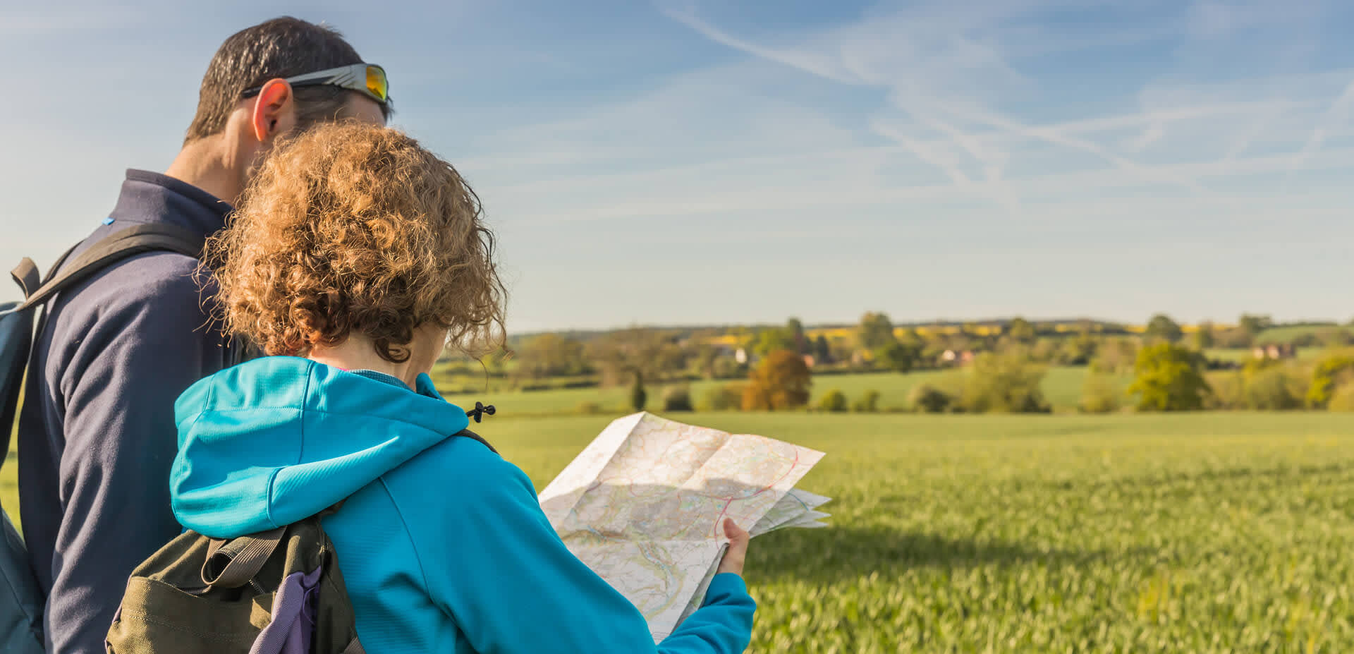 Man and lady exploring through green field with a map in hand