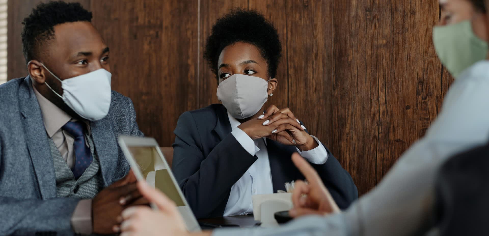 Business people hold a discussion around a table while wearing face masks