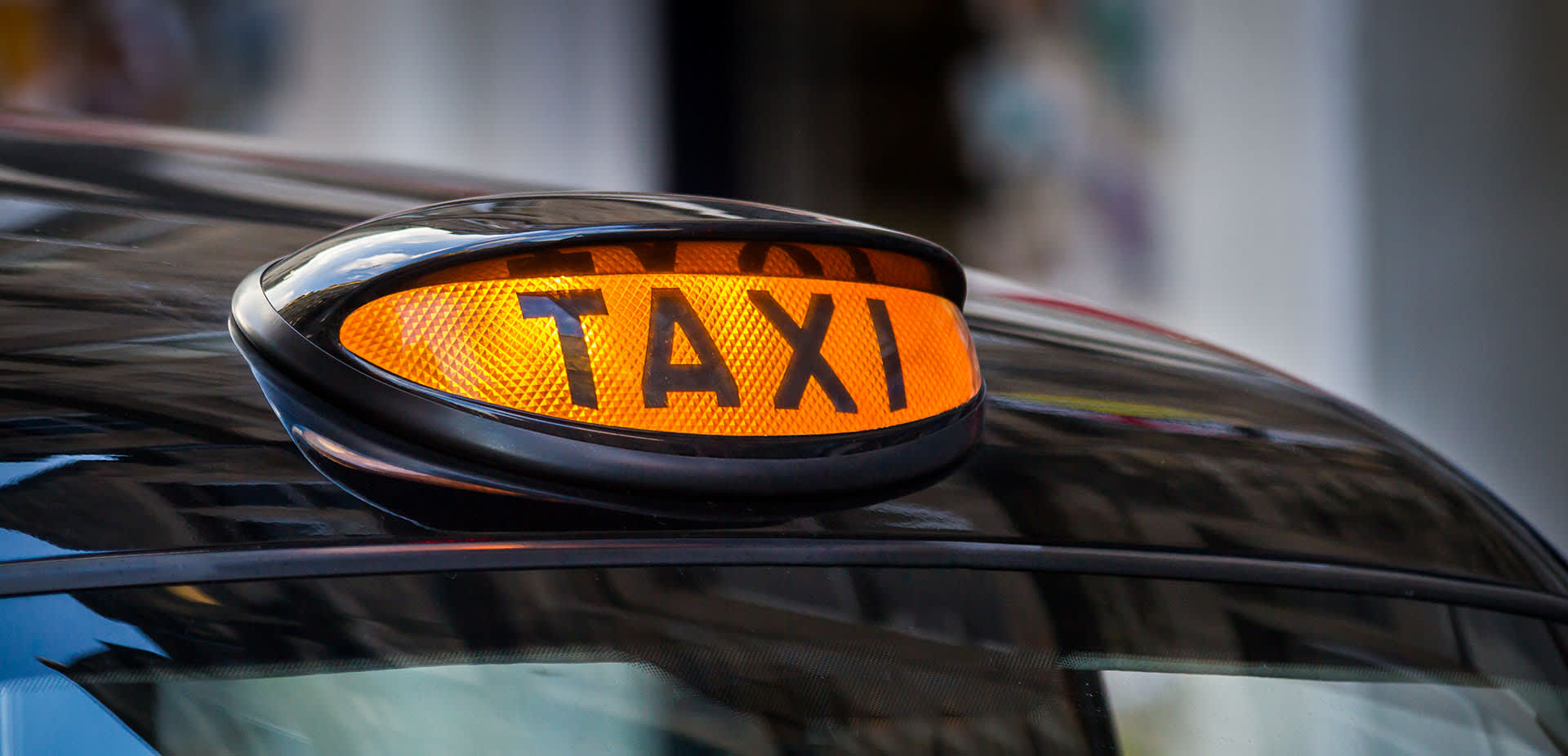 Lit up taxi sign on top of a black cab