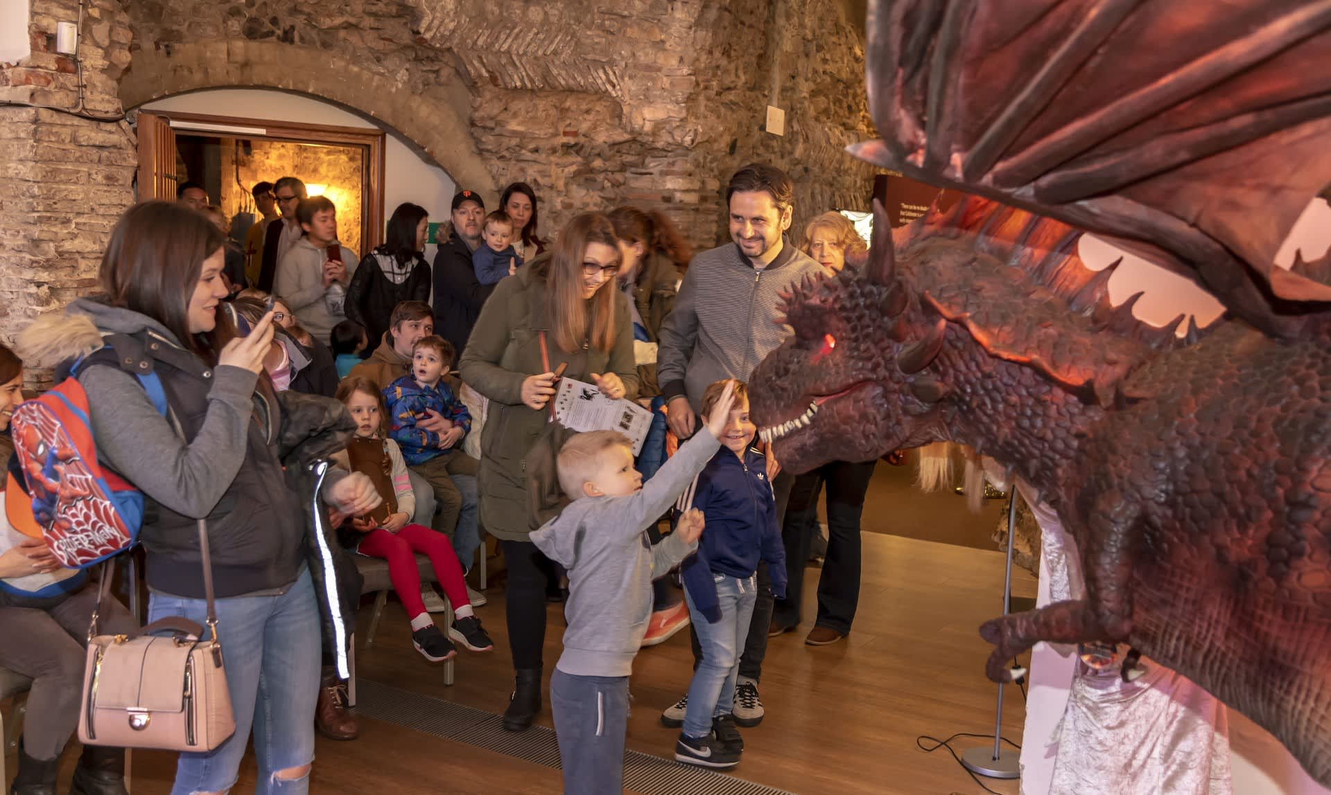 A child touches a dragon in Colchester Castle, surrounded by friends and family.
