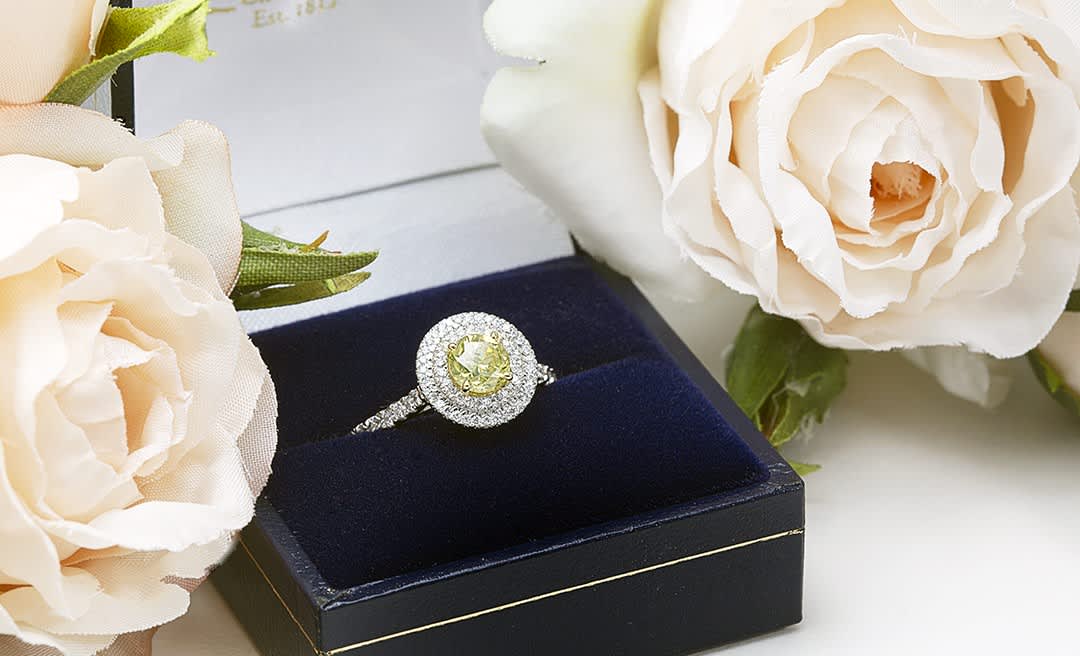 A stunning engagement ring in a box surrounded by pale pink roses
