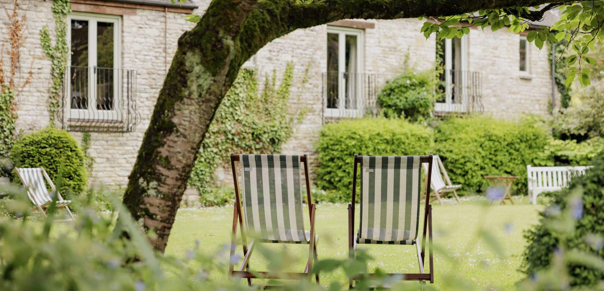 External shot of Bay Tree Cotswold Inn in Burford with deck chairs under a tree