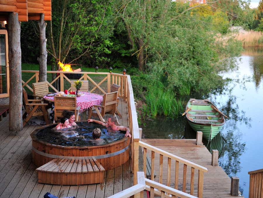 Family in hot tub on the deck of a lake side lodge at Log House Holidays