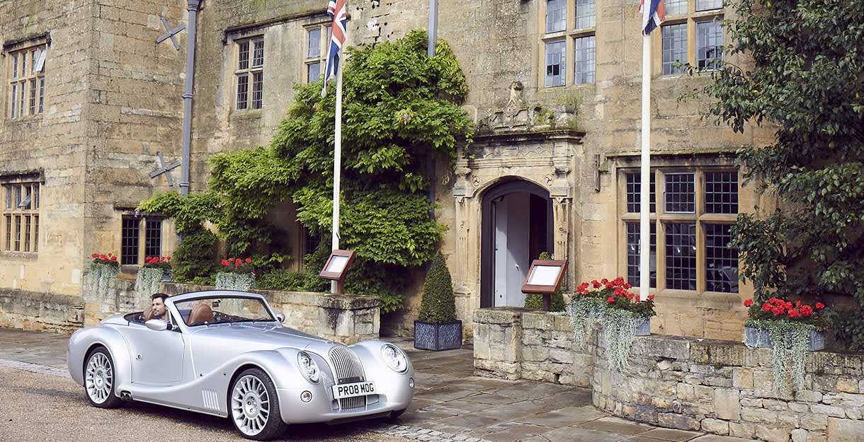 A vintage car parked in front of the Cotswold stone entrance to The Lygon Arms in the Cotswolds