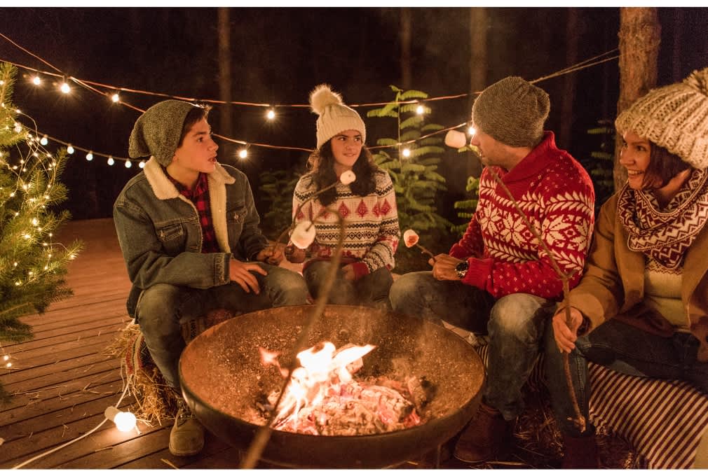 family sitting around wood burning pit and toasting marshmallows