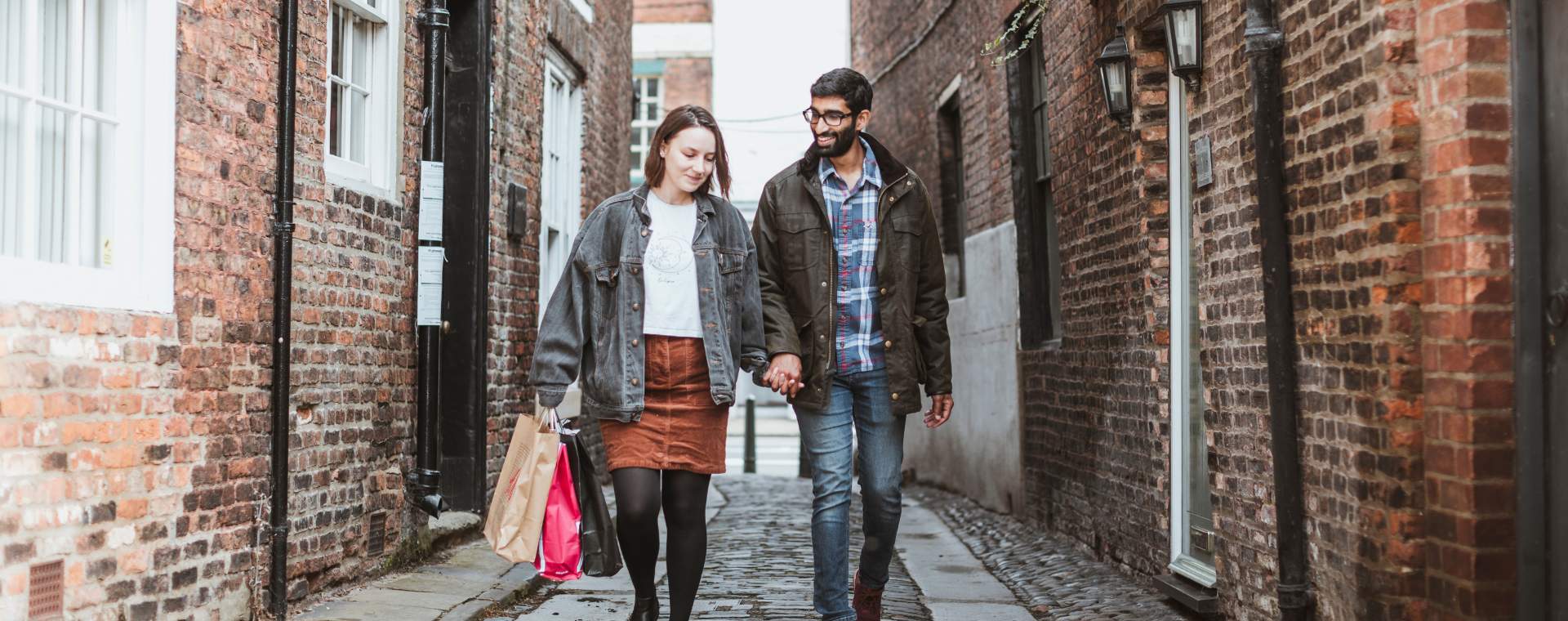 A couple walking hand-in-hand down one of Beverley's narrow cobbled streets, carrying shopping bags.