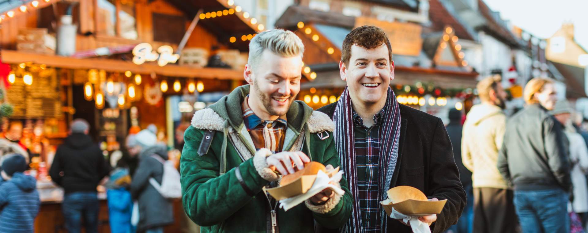 Two men stood in front of illuminated food stalls at the Beverley Festival of Christmas in East Yorkshire, about to tuck into carvery sandwiches