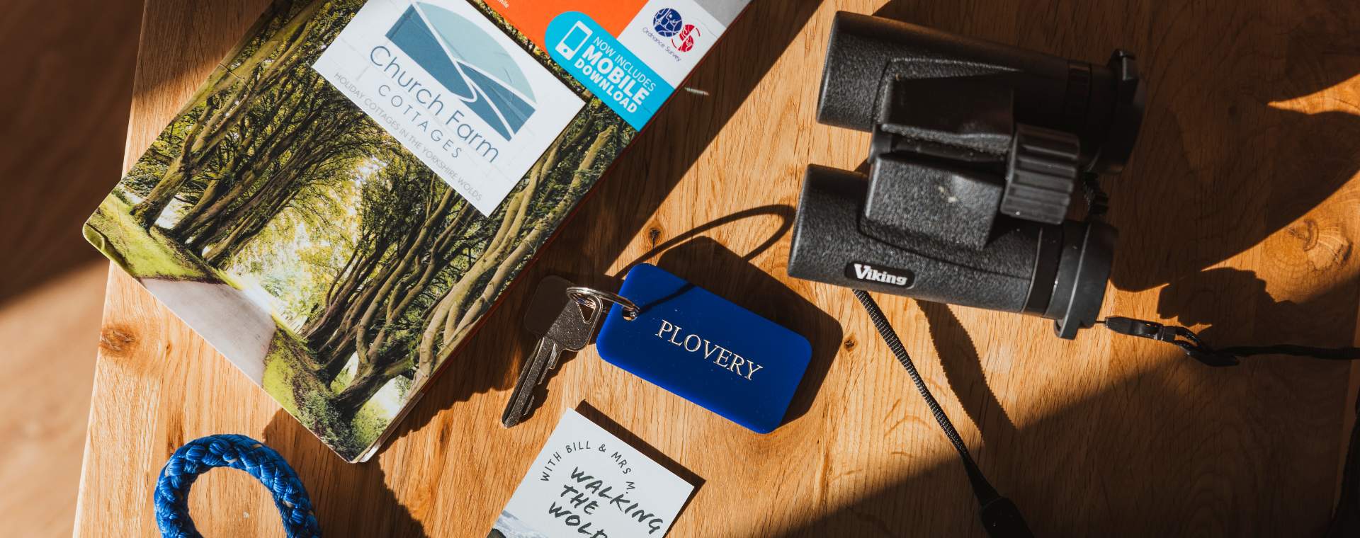 An overhead shot of the table, including an OS map, pair of black binoculars, Plovery room tag and key, and Church Farm/ Walking the Wolds business cards.