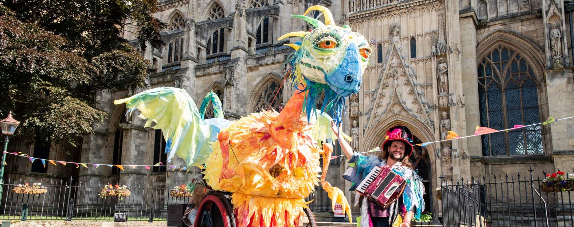 A giant puppet of a dragon next to a man playing an accordion in front of Beverley Minster in East Yorkshire