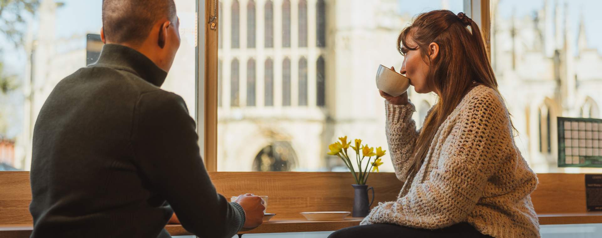 A couple sat drinking coffee in Gemini Chocolate in Beverley with views looking out onto St Mary's Church.