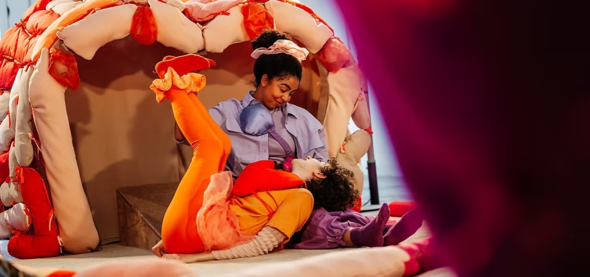 A woman dressed up in costume cradles another actor in her knee in front of a foam brain.
