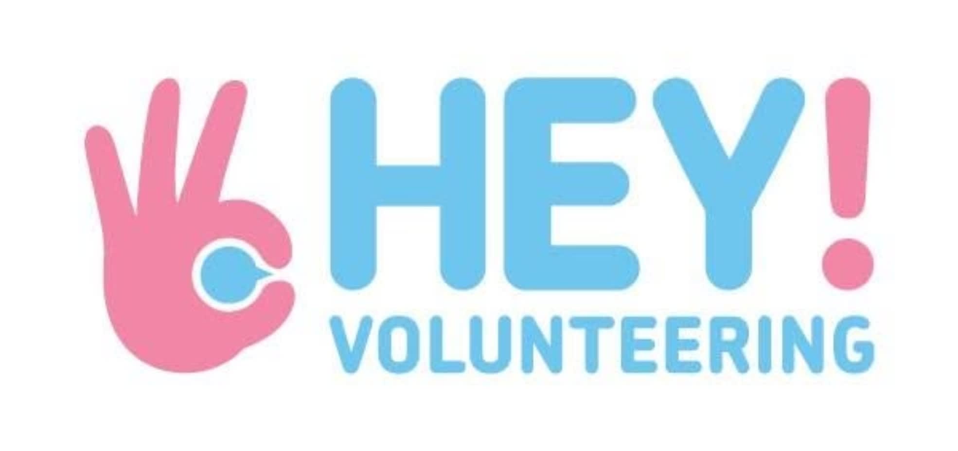 The Hey volunteering logo in blue and pink lettering. A hand symbol in pink is at the left side.