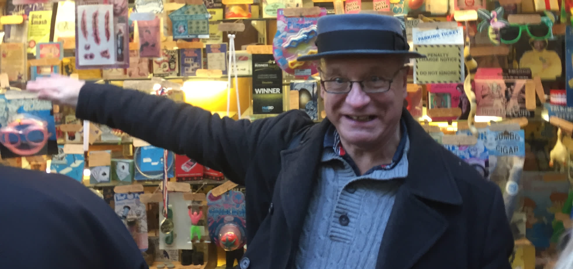 Local tour guide standing beside Hulls colourful vintage joke shop display filled with 4 novelty items and quirky memorabilia