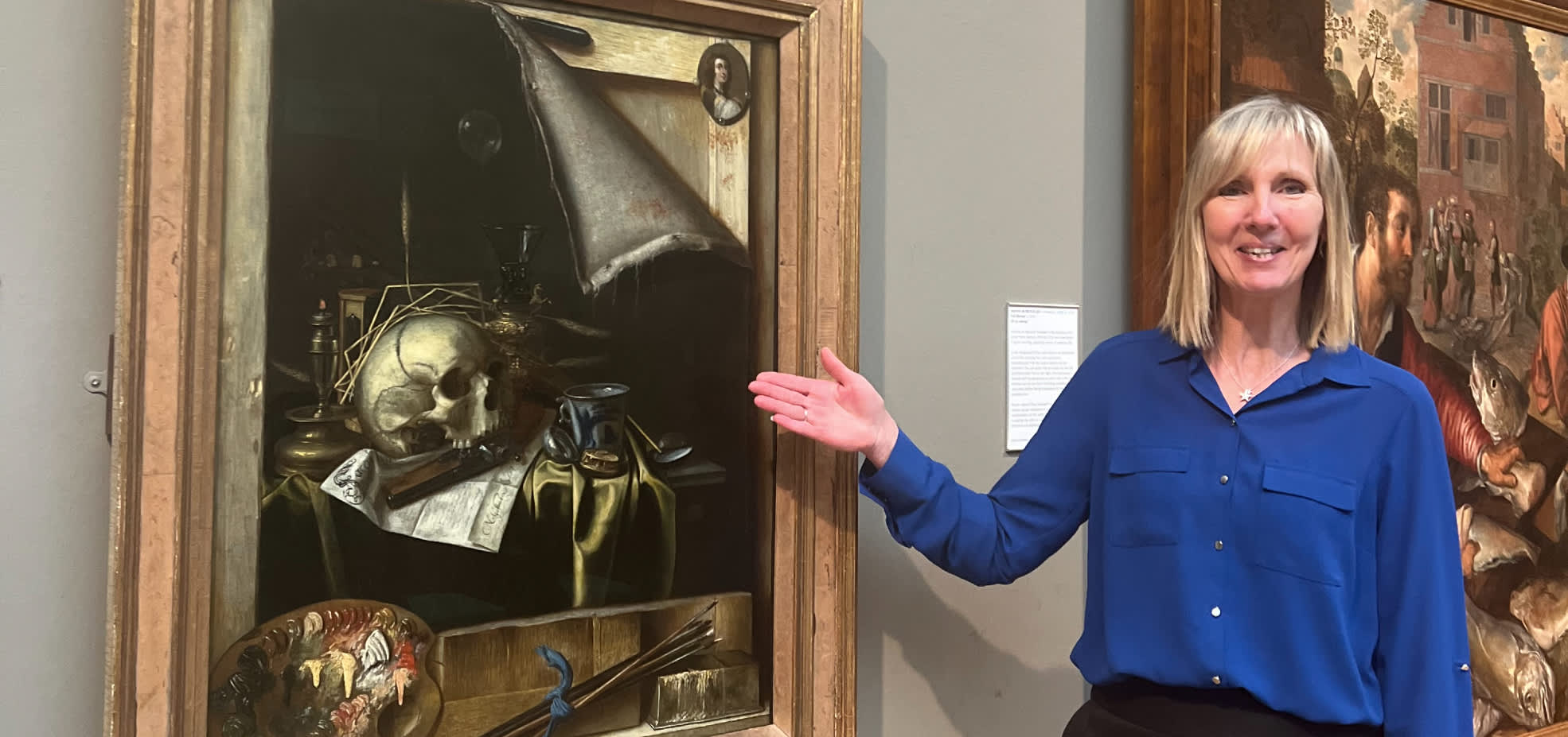 A guide presenting a framed still‑life painting inside Ferens art gallery, Hull, with detailed artwork and exhibition labels visible on the wall.