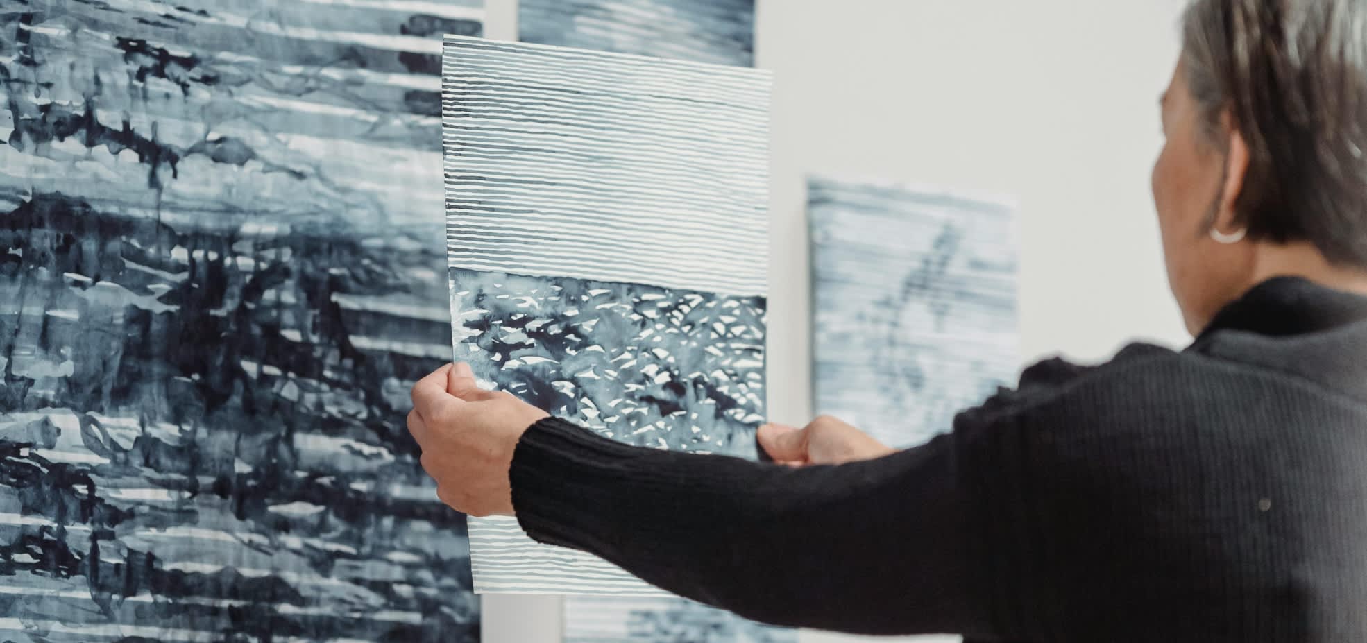 A woman hangs grey portraits on a gallery wall in preparation for an exhibit