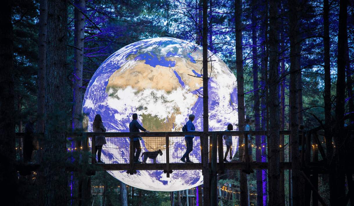 A giant, floating Earth amongst trees with a walkway of people looking on