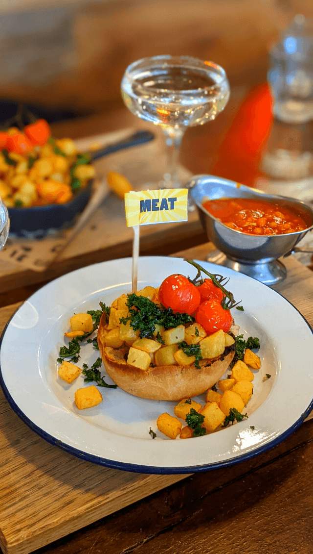 A breakfast pie covered in tater tots and tomatoes. The pie is served on a white plate on a wooden board.
