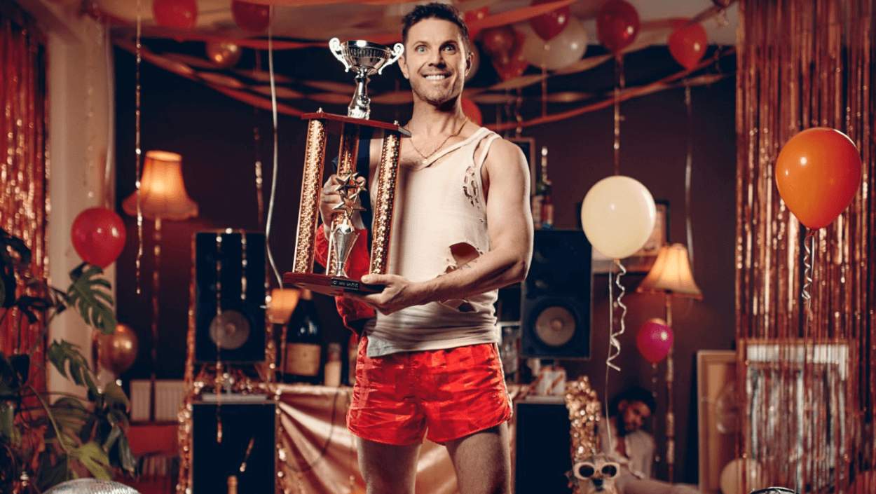 Jake Shears stood a room full of balloons holding a trophy
