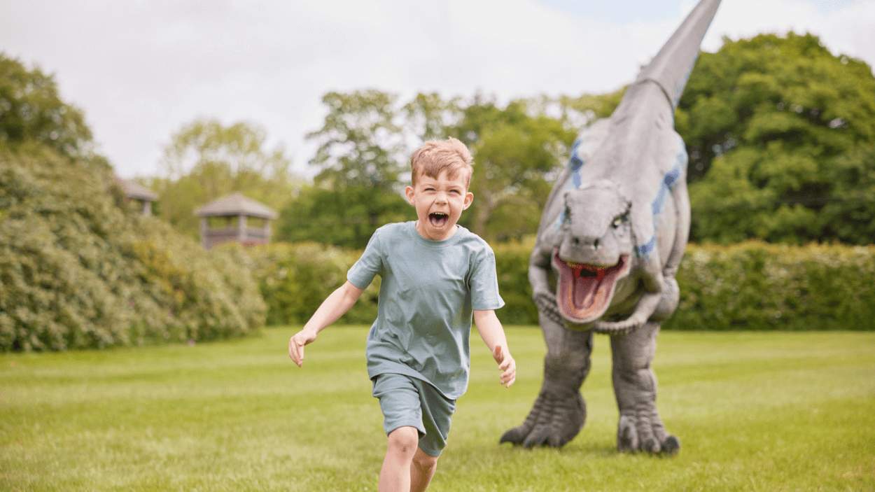 A young boy being chased by a fake dinosaur.