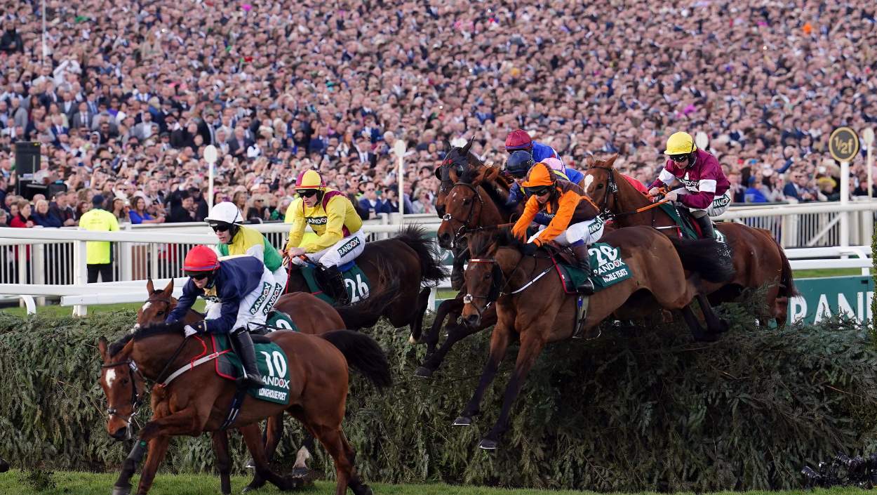Jockeys and their horses making a jump over a fence at the Grand National Festival