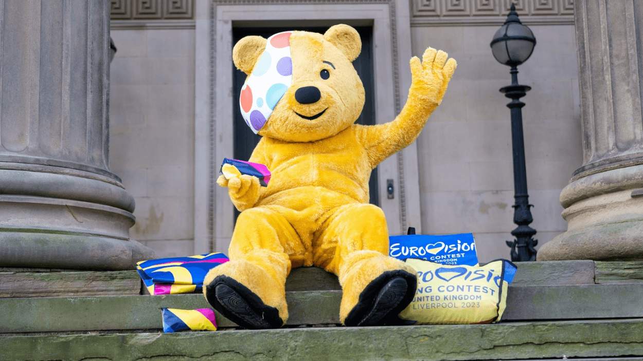 Pudsey bear sitting on some steps at St George's Hall with some bags next to them.