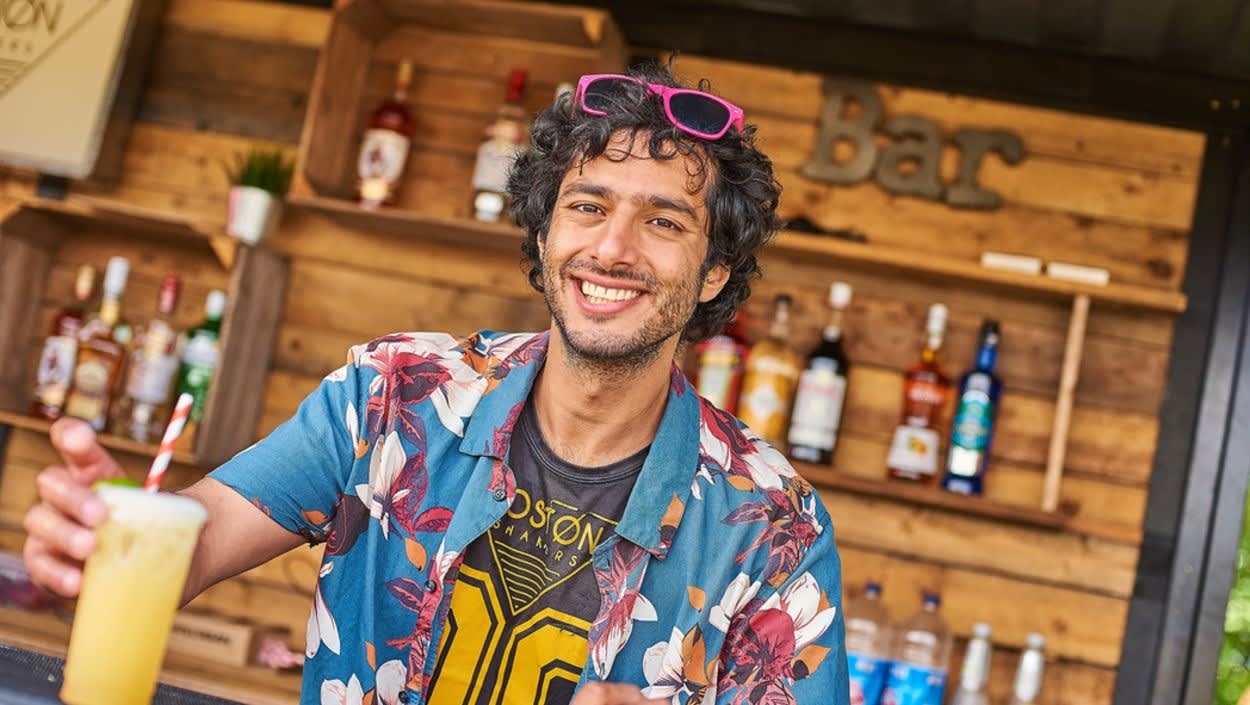 A man in a wooden chalet making cocktails, smiling at the camera